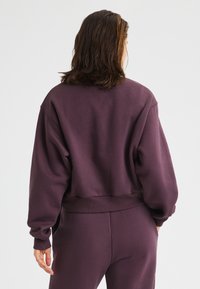 Felpa pullover color bordeaux con maniche lunghe, polsini larghi e vestibilità comoda. Presenta un orlo a coste e una texture morbida.