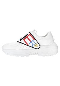 Baskets blanches de sport avec une semelle épaisse, dotées d'une large bride diagonale portant un texte rouge, noir et bleu, et des accents en tissu texturé.