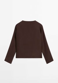Chemise à manches longues marron foncé avec col rond, design simple, posée à plat avec les manches étendues sur un fond blanc.