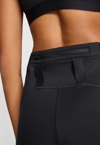 Μαύρο αθλητικό κολάν με ψηλό ζωνάρι μέσης, υφημένα ριμπ μοτίβα και τσέπη με φερμουάρ στο πίσω μέρος, με ραφές flatlock.