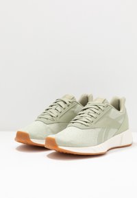 Světle zelené sportovní boty s texturovaným svrškem, tkaničkami a béžovou gumovou podrážkou. Vyznačují se štíhlým designem a decentním logem na boku.