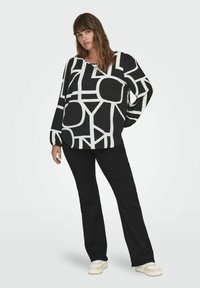 Černobílá vzorovaná blůza s oversized rukávy, v kombinaci s černými kalhotami a světlými teniskami. Hladká textura, uvolněný střih.