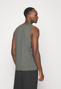 Grå ermeløs topp laget av strikket stoff, med rund halslinning og avslappet passform, parret med mørke shorts. Enkel, minimal design.