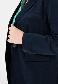 Granatowa marynarka z korduroju z pojedynczym guzikiem, wyraźnymi klapami i boczną kieszenią; widoczna tekstura materiału na powierzchni.