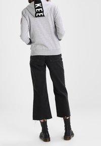 Grauer Kapuzenpullover mit schwarzem "KEEP"-Schriftzug auf der Kapuze, kombiniert mit schwarzen verkürzten Hosen und schwarzen Knöchelstiefeln.