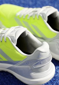 Pair of neon yellow and white athletic shoes with laces, shown close-up on a blue textured surface.