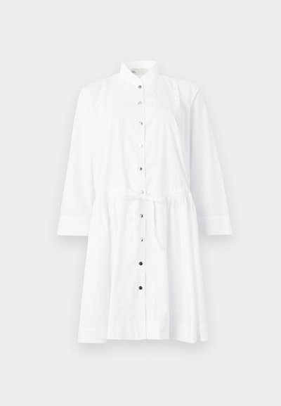 Valge nööbidress, millel on mandariini krae, pikad varrukad, vöökoht, mida saab kinni siduda, ning kontrastsed mustad nööbid esiosas.