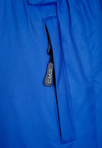 Bright blue outdoor pants feature a zipper pocket with a black pull tab marked "CMP," showing a smooth texture and durable fabric.