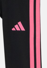 Joggers noirs avec des rayures latérales roses et un logo Adidas rose. Confectionnés dans un tissu lisse et extensible avec une coupe ajustée.