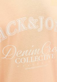 Gros plan sur un tissu beige avec un texte blanc indiquant 'Jack & Jones Denim Creation Collective Worldwide Established Nineteen Ninety'