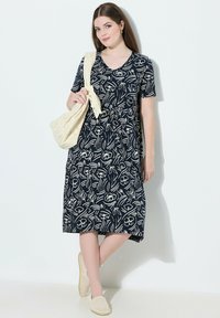 Laivansininen kukkakuosiset mekko, jossa on lyhyet hihat, v-pääntie ja rento malli. Yhdistettynä vaaleaan laukkuun ja vaaleisiin liukuviin kenkiin.