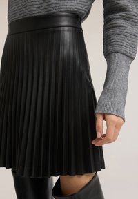 Svart plisserad kjol i konstläder med bred midjerem. Kompletteras med en grå ribbstickad långärmad topp och en svart stövel som går över knäet.