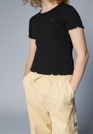 Czarna, żeberkowana koszulka z krótkim rękawem z falbaniastym dołem i małym haftowanym logo, w połączeniu z luźnymi beżowymi spodniami cargo.