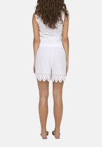 Weißes besticktes ärmelloses Oberteil mit gewellten Säumen, dazu Shorts mit Lochdesign, elastischem Bund und flachen Sandalen.