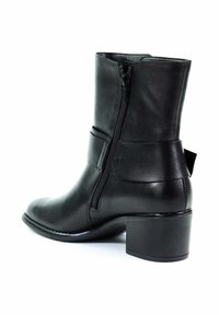 Bottine en cuir noir avec fermeture éclair latérale, sangle décorative et talon carré sur fond blanc.