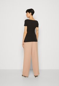 Top ajustado negro con mangas cortas, combinado con pantalones de pierna ancha en rosa pálido. Tela suave, diseño minimalista, sin estampados. Zapatos de tacón visible.