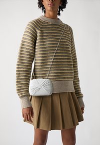 Maglione a righe in giallo smorzato e grigio, abbinato a una gonna plissettata color oliva. Una piccola borsa a tracolla argentata con un motivo testurizzato.