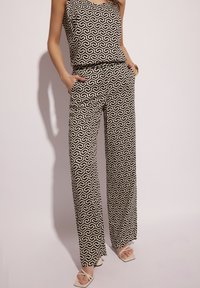 Czarny i kremowy zestaw w wzory składający się z bezrękawnikowego topu i spodni o szerokich nogawkach z kieszeniami, wykonany z gładkiego materiału. Całość dopełniają sandały z kwadratowymi noskami.