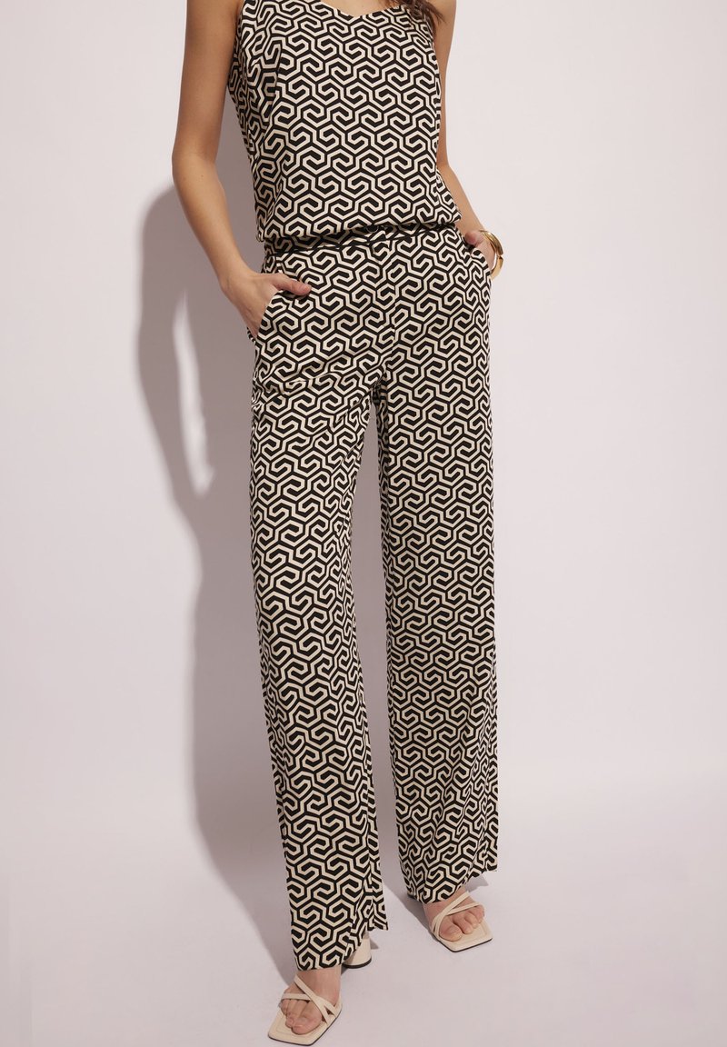 Czarny i kremowy zestaw w wzory składający się z bezrękawnikowego topu i spodni o szerokich nogawkach z kieszeniami, wykonany z gładkiego materiału. Całość dopełniają sandały z kwadratowymi noskami.