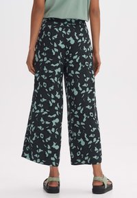 Vloeiende zwarte culottebroeken met een mintgroen bloemenpatroon; soepele stof; enkel-lang; gecombineerd met zwarte plateausandalen.