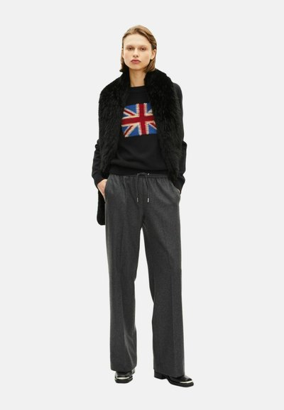 Czarny sweter z wzorem Union Jack, warstwowy z kołnierzem z sztucznego futra. Szare szerokie spodnie i czarne botki za kostkę dopełniają stylizację.