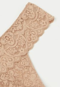 Nude kantstof met bloemmotieven en geschulpte randen, die ingewikkelde textuur en detail toont in een delicaat ontwerp.