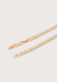 Χρυσό βραχιόλι με κυκλικές ρυθμίσεις, καθεμία φιλοξενεί μία κεντρική διαυγή πέτρα περιβαλλόμενη από μικρότερα κρύσταλλα, τοποθετημένο επίπεδα σε λευκή επιφάνεια.