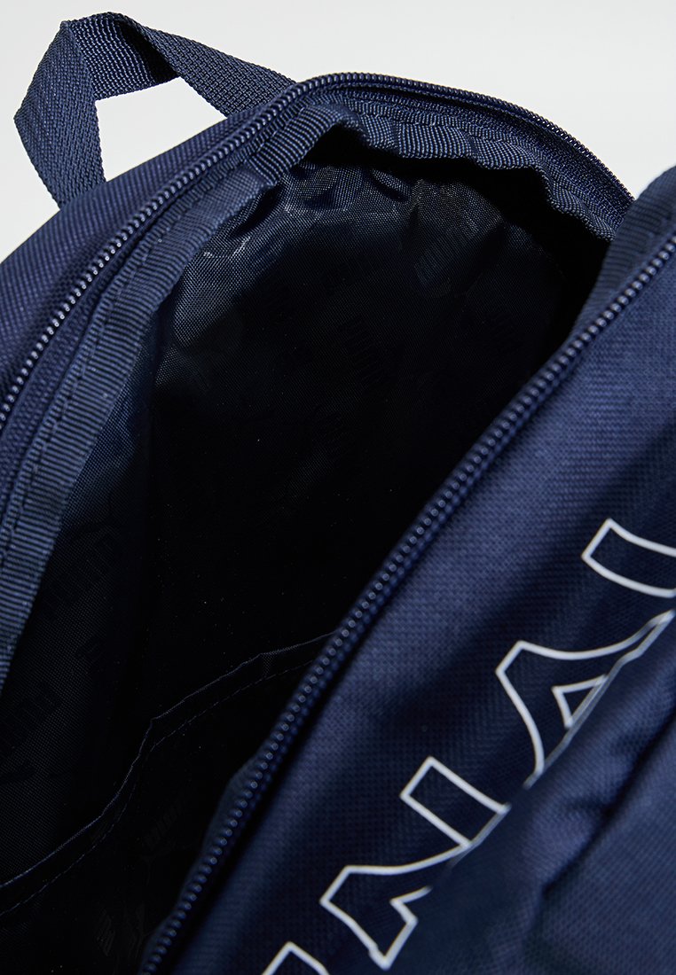 Mochila azul marino con una tela texturizada, que cuenta con una abertura con cremallera y un forro interior. Acentuada con letras de logotipo en blanco en el costado.