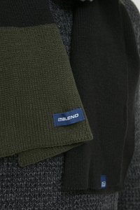 Strickschal mit dunkelgrünen und schwarzen Abschnitten. Verfügt über eine strukturierte Webart und ein kleines blaues Etikett mit dem "BLEND"-Logo. Entwickelt für Wärme.
