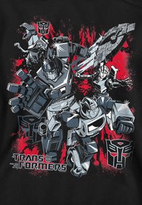 Graphic t-shirt featuring Transformers characters in black, gray, and red colors, with a splatter design and 'Transformers' text at the bottom.