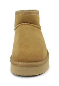 Stivale alla caviglia in suede beige con punta arrotondata, cuciture minime e suola piatta e testurizzata. Presenta un morbido rivestimento interno.
