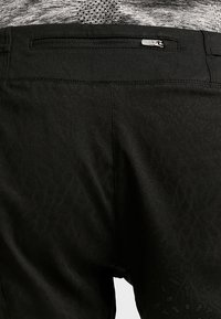 Pantalones negros con un patrón texturizado, que incluyen un bolsillo trasero con cremallera. La tela tiene un brillo sutil y un acabado suave.