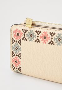 Cartera de cuero crema con bordado floral en rosa y azul, con herrajes dorados y una superficie texturizada. Cierre de cremallera en la parte superior.