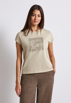Beige bomulls-t-shirt med kortärmar, som har en texturerad fyrkantig design med texten "QUIET SENSES" i en kontrasterande färg.
