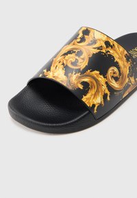 Sandalia tipo sandalia negra con parte superior brillante con un patrón ornamentado dorado en espiral y plantilla negra texturizada. Diseño sencillo de deslizar.