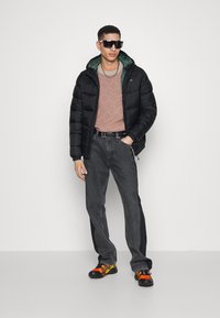 Svart puffjacka med grön insida, mönstrad orange tröja, grå jeans och flerfärgade sneakers. Stora solglasögon fulländar looken.