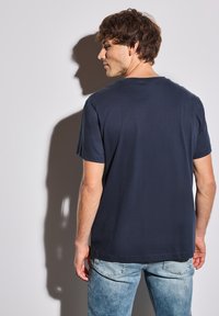 T-shirt en coton bleu marine à manches courtes, col ras du cou et texture lisse, associé à un jean bleu clair, vu de dos.