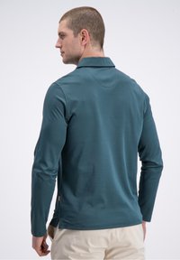 Polo marškinėliai ilgomis rankovėmis žalsvos spalvos, su faktūruotu paviršiumi, klasikinio tipo apykakle ir šoninėmis skeltukėmis patogiam judėjimui.