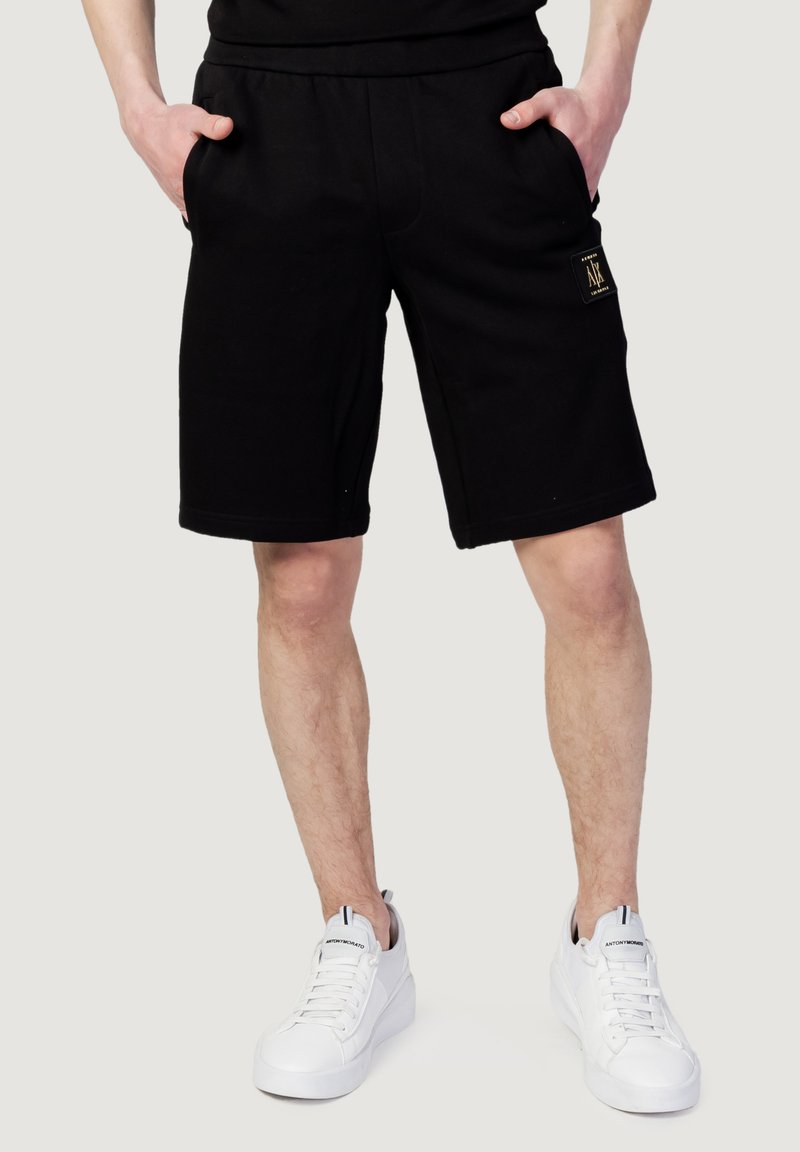 Shorts in cotone neri con vestibilità rilassata, caratterizzati da due tasche laterali e un piccolo logo. Abbinati a sneakers bianche.