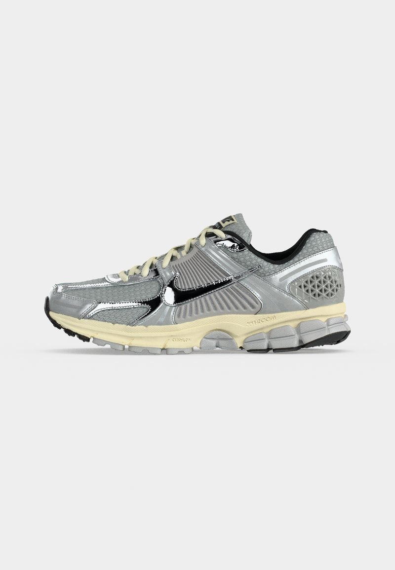 Zapatilla de correr Nike plateada y negra con suela beige, empeine de malla y sintético, y logo swoosh negro en el lateral, vista desde el lado exterior.