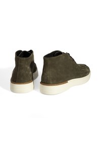 Olijfgroene suède hoge schoenen met een witte rubberen zool, voorzien van een tan accent rondom de zool en ronde veters. Textuur oppervlak.