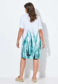 Kurzärmeliges Kleid aus weißem Stoff mit einem aquarellartigen Muster aus tealfarbenem und grünem Gras im unteren Bereich.