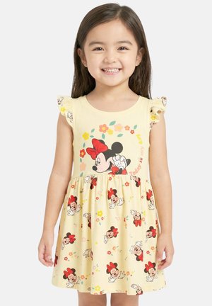 Jeune fille souriante, portant une robe jaune avec des manches à volants et des imprimés rouges Minnie Mouse et fleurs.