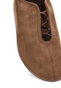 Zapato de ante marrón con puntera redondeada, que presenta un detalle de costura decorativa a lo largo de la abertura y un cierre de cordones.