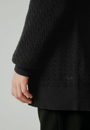 Schwarzer Strickpullover mit einem Kabelmuster, gerippten Bündchen und Saum. Verfügt über ein kleines Logodetail nahe dem Saum. Die Textur wirkt weich und warm.