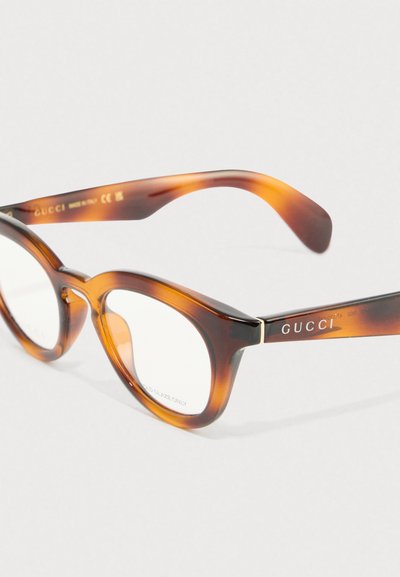 Ochelari cu rame dintr-un material scoică, cu un design în formă de ochi de pisică, având acetat groase, lentile transparente și un accent subtil de aur pe bradă.