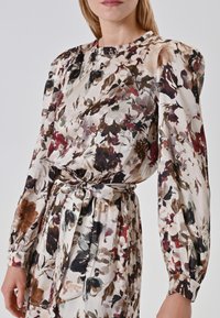 Bloemenjurk van lichte stof in een mix van bordeaux, bruin en roomkleur, met pofmouwen en een getailleerde riem.