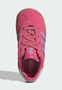 Sapatilha de camurça rosa com riscas azuis, biqueira redonda, língua texturizada e sola de borracha clara. Apresenta logótipo na língua e na palmilha.