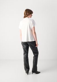 Witte korte mouwen top, ontspannen pasvorm, gecombineerd met zwarte leren broeken. Opvallende textuur en op maat gemaakt ontwerp complementeren de outfit.