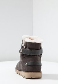 Tumman harmaa nappa-ankalakki, jossa on tekoturkisel lining, hihnadesign, ovali hopeinen varuste ja teksturoitu vaaleanruskea kumipohja.